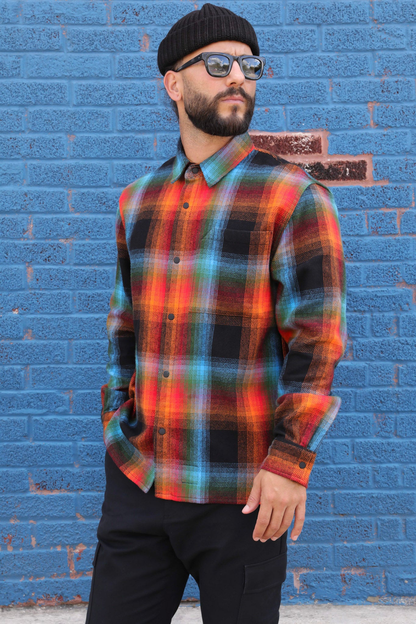 Man wearing a colorful plaid shirt against a blue brick wall