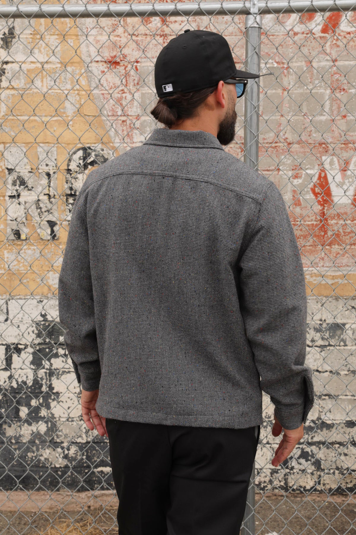 Man wearing a gray wool Signature zip-up jacket and black cap standing against a textured wall.