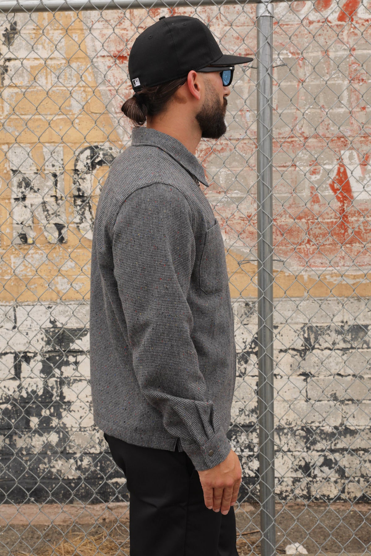Man wearing a gray wool Signature zip-up jacket and black cap standing against a textured wall.
