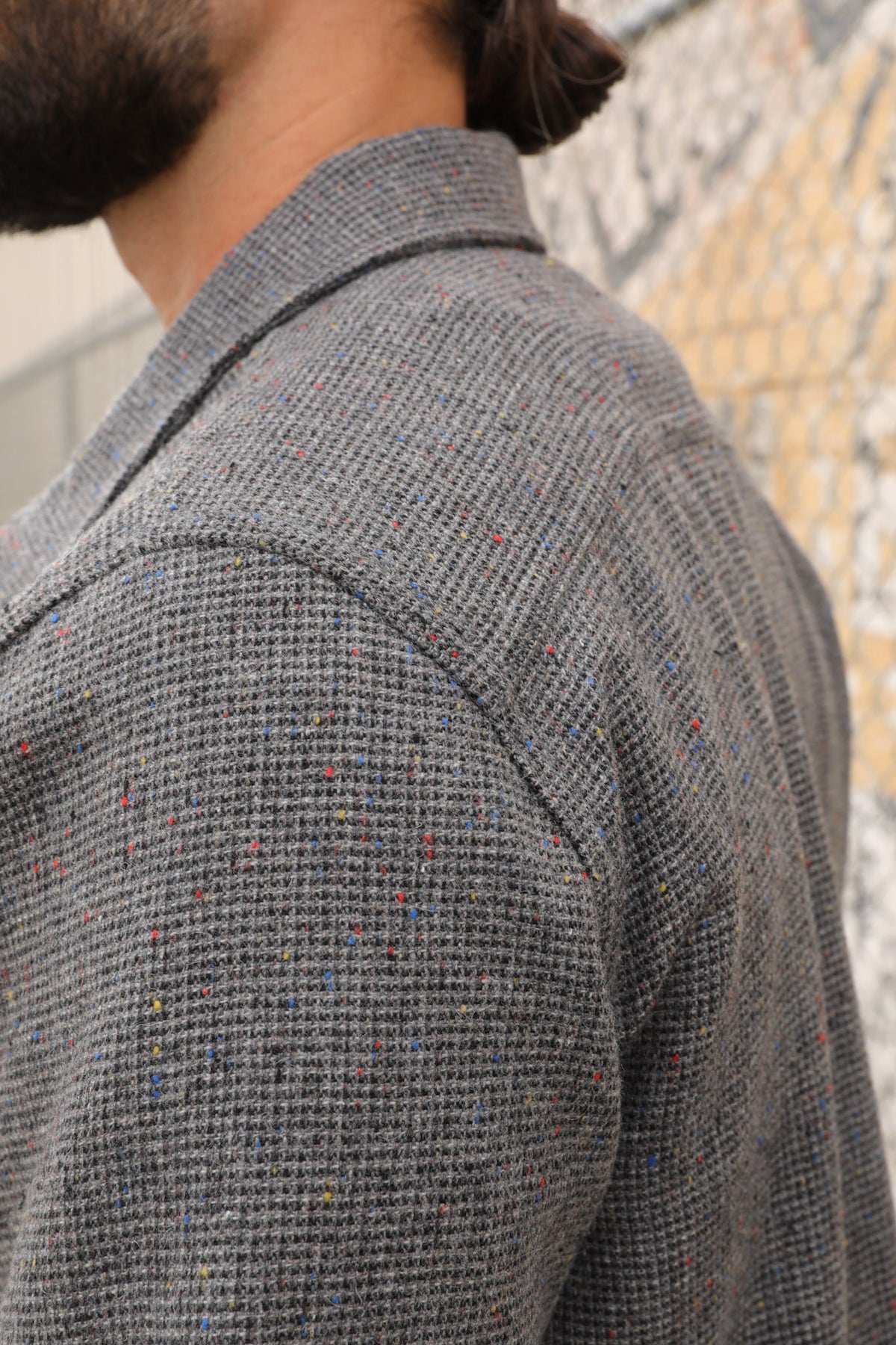 Man wearing a gray wool Signature zip-up jacket and black cap standing against a textured wall.