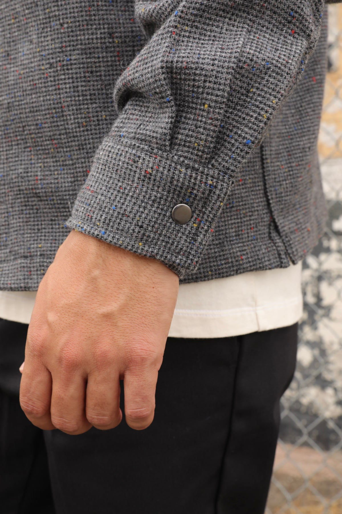 Man&#39;s sleeve wearing a gray wool Signature zip-up jacket and black cap standing against a textured wall.