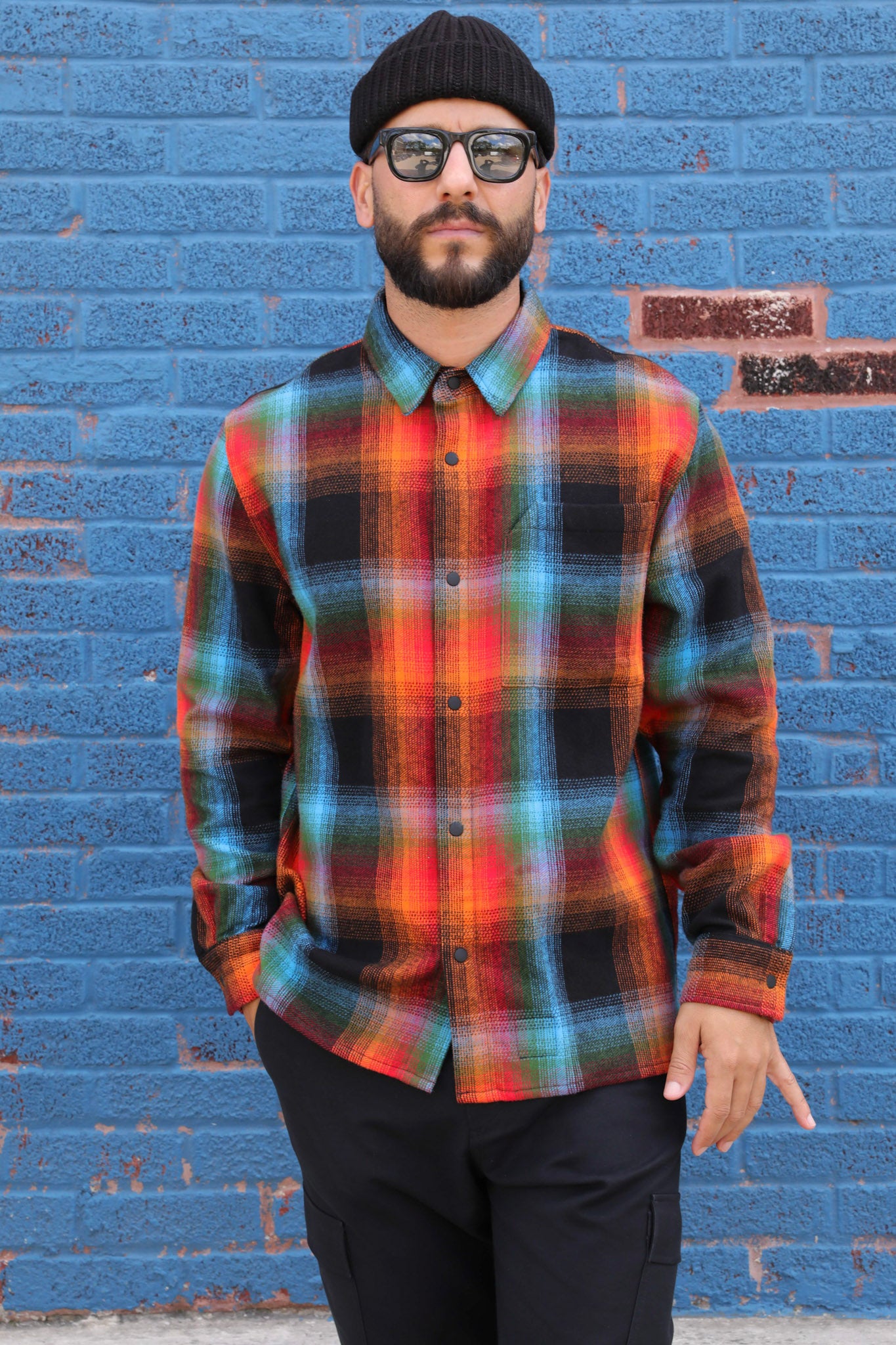 Man wearing a colorful plaid shirt against a blue brick wall