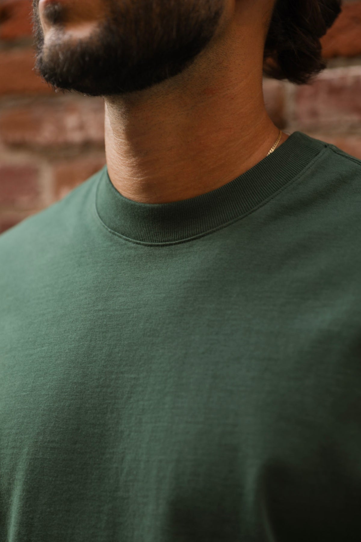 Close-up of a person wearing a green t-shirt against a brick wall.