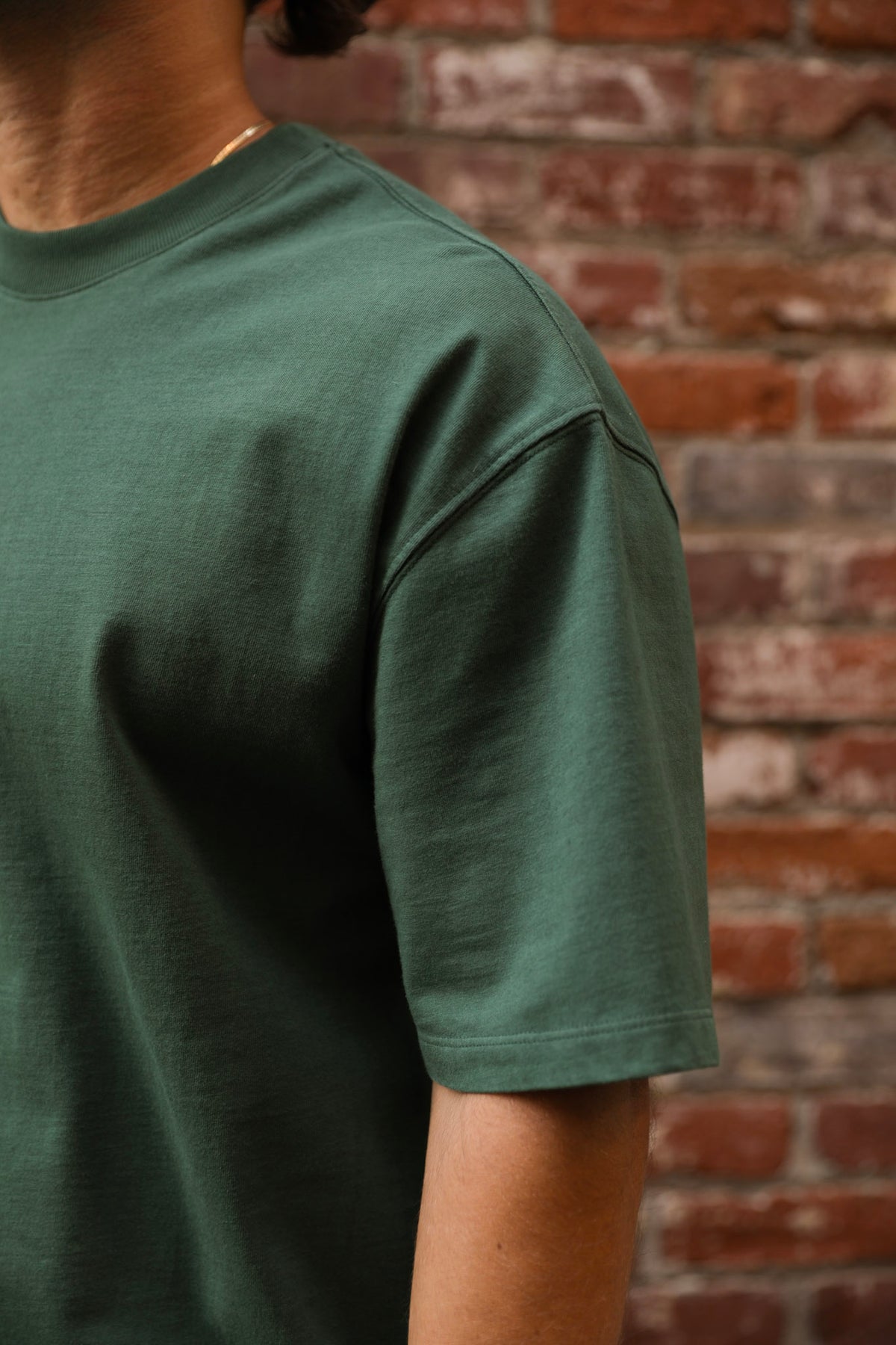 Person wearing a green t-shirt against a brick wall