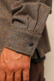 Close-up of a person's hand wearing a brown tweed jacket with a rolled cuff showing a black button closure.