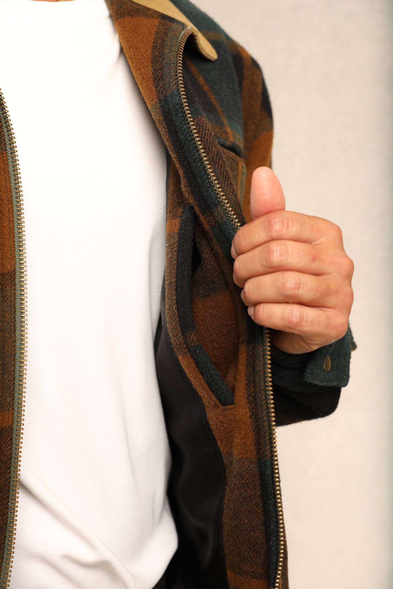 Close-up of a person wearing a brown and black plaid zip-up jacket over a white shirt, with the hand holding the jacket open.