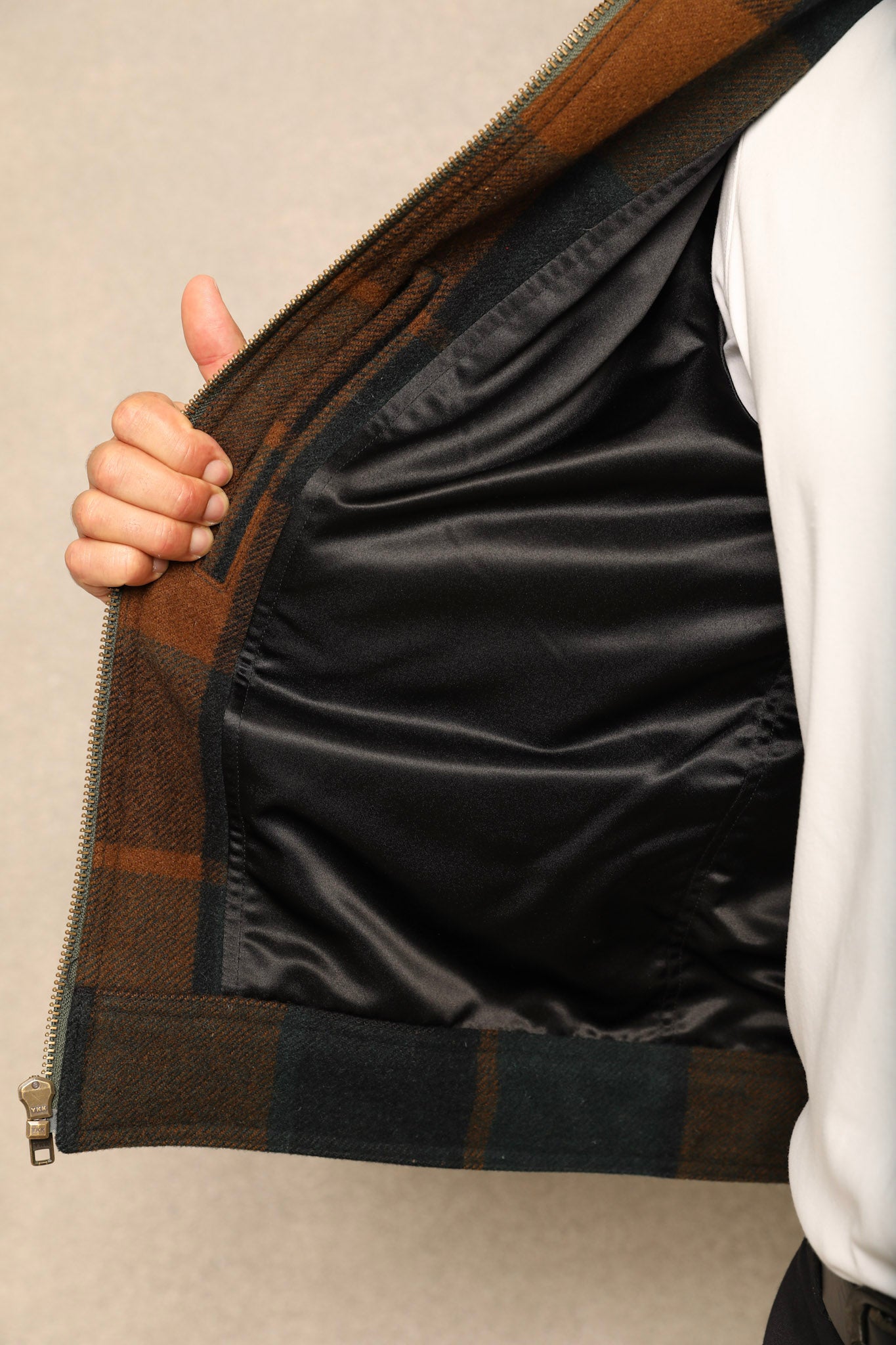 Close-up of a person opening a zippered jacket to show a black satin-lined interior and brown plaid outer fabric.
