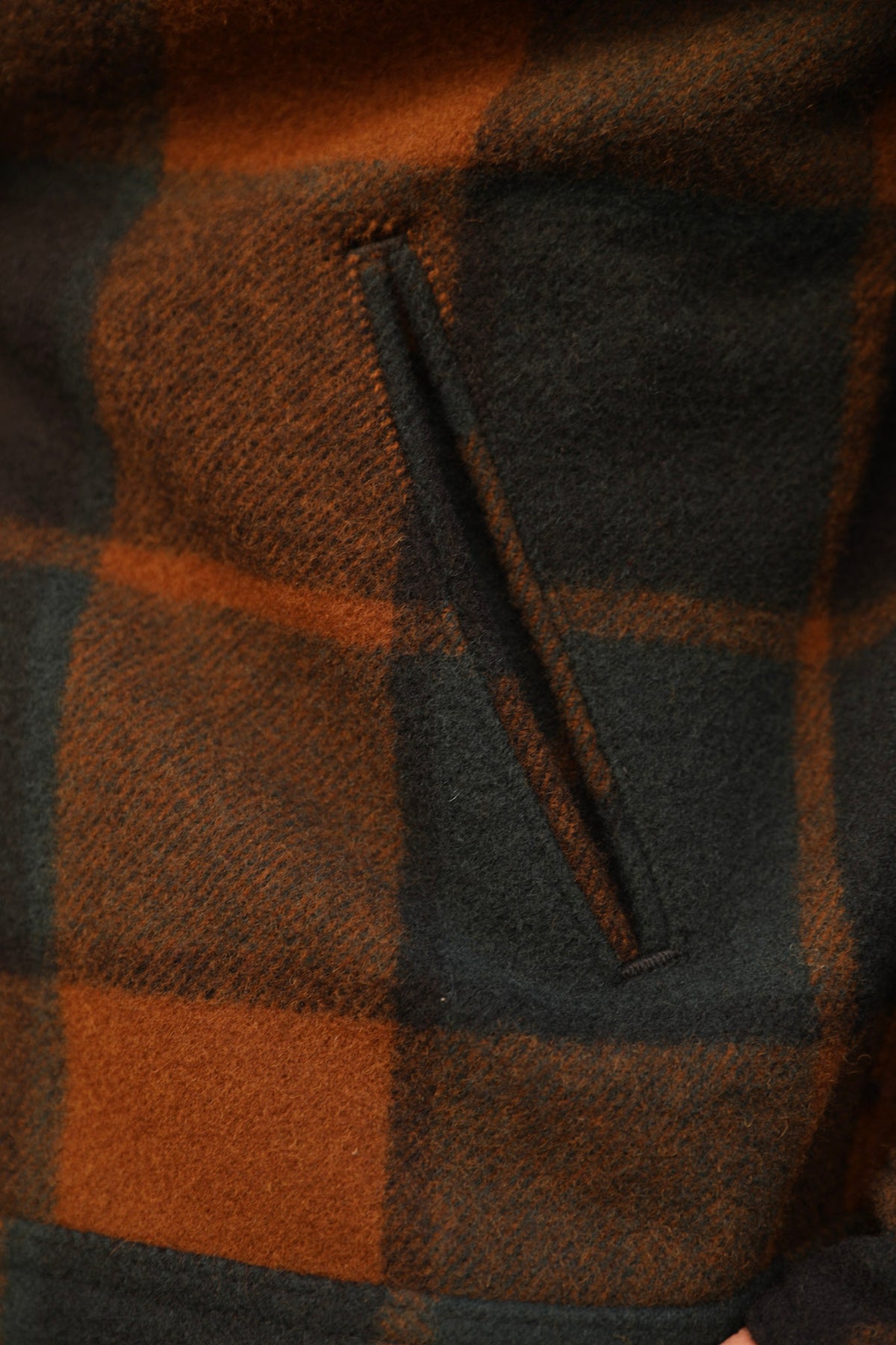 Close-up of a plaid wool fabric in dark brown and black, featuring a diagonal welt pocket.