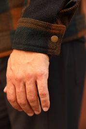 Close-up of a person's hand wearing a dark brown and black plaid wool jacket with a buttoned cuff.