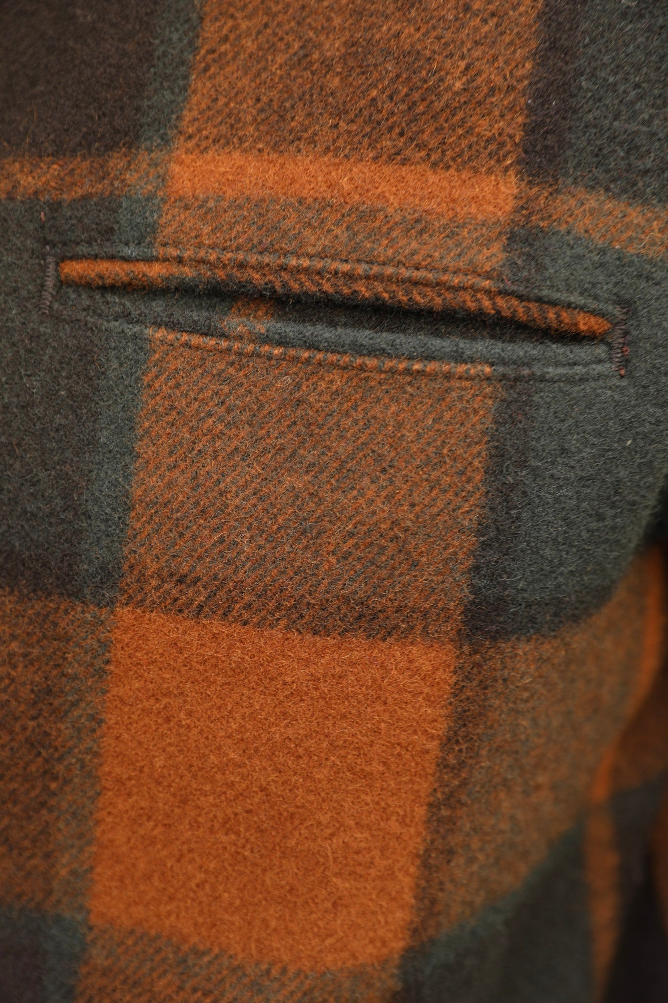Close-up of a plaid wool fabric with a pocket, featuring a pattern of rust orange and dark charcoal gray.