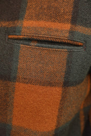 Close-up of a plaid wool fabric with a pocket, featuring a pattern of rust orange and dark charcoal gray.