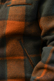 Close-up of a textured plaid fleece jacket in dark gray and burnt orange, showing a pocket and fabric weave detail.