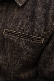 Close-up detail of a dark indigo textured fabric denim jacket, showing a horizontal welt pocket with double-stitched trim.