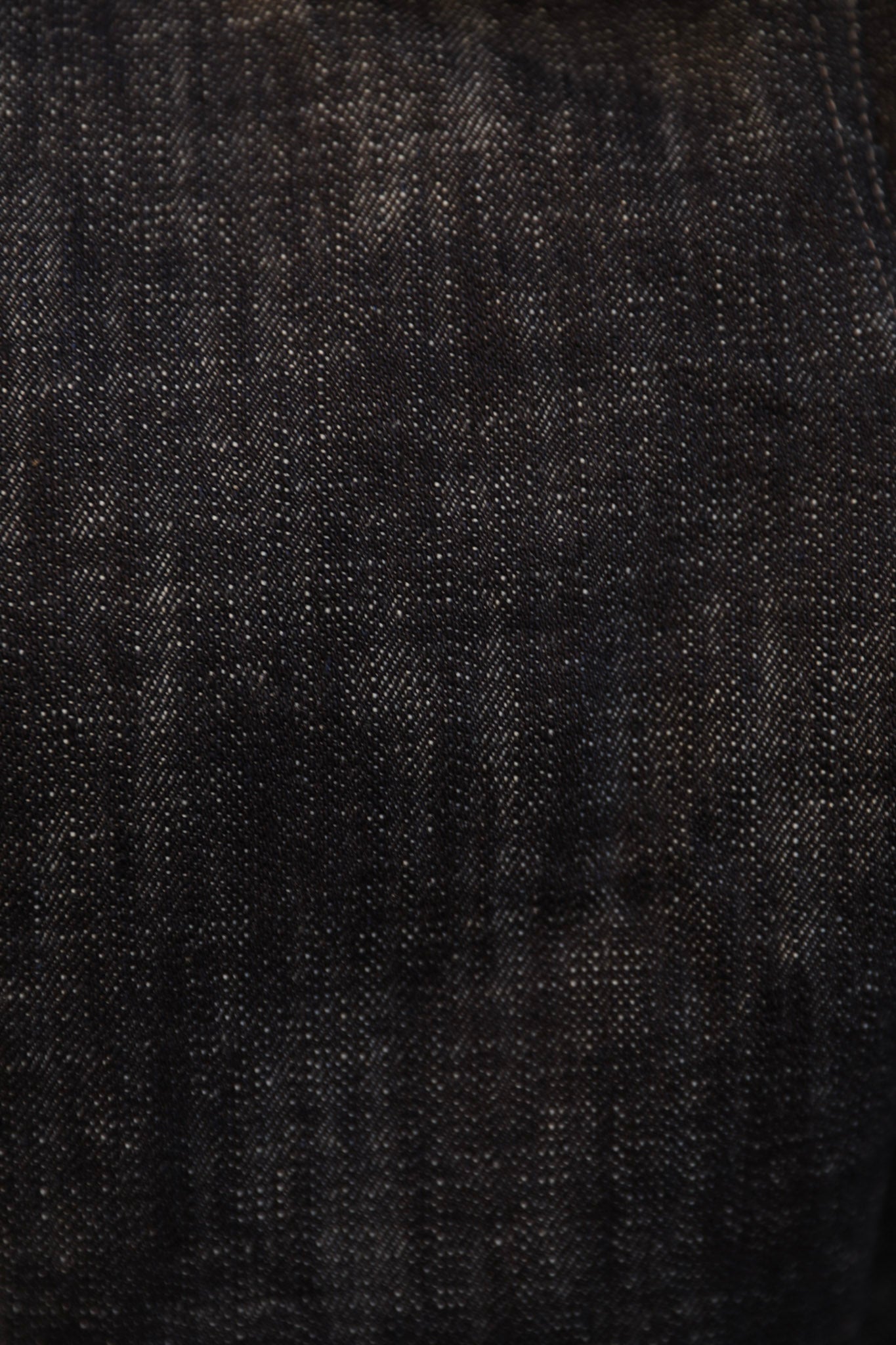 A close-up texture shot of dark indigo denim fabric, showing the detailed weave and subtle fading.