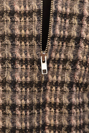 Close-up of a textured tweed zipper garment, showing a black, gray, and beige patterned fabric with a silver metal zipper pull.