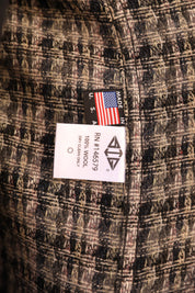 Close-up of a plaid wool fabric garment with a sewn-in label showing a black 'MADE IN USA' tag with an American flag and a white size/variant label reading RN #146579, 100% Wool, and A4A.