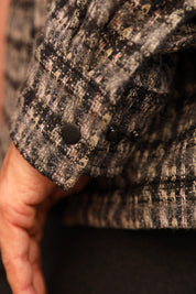 Close-up of a textured tweed jacket sleeve with a dark button, worn by a person whose hand is visible.