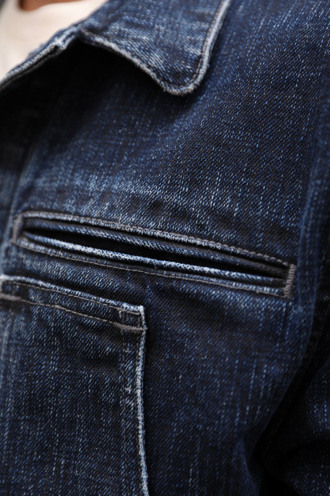 Close-up of dark indigo denim fabric showing a pocket seam and stitched collar detail.