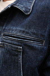 Close-up of dark indigo denim fabric showing a pocket seam and stitched collar detail.