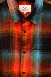 A close-up of a plaid button-up shirt with a vibrant multicolor pattern featuring orange, red, black, green, and blue. The collar label shows the brand 'New York & Main'.