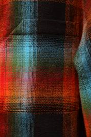 A close-up of a plaid fabric pattern with intersecting stripes in red, orange, teal, green, and black.