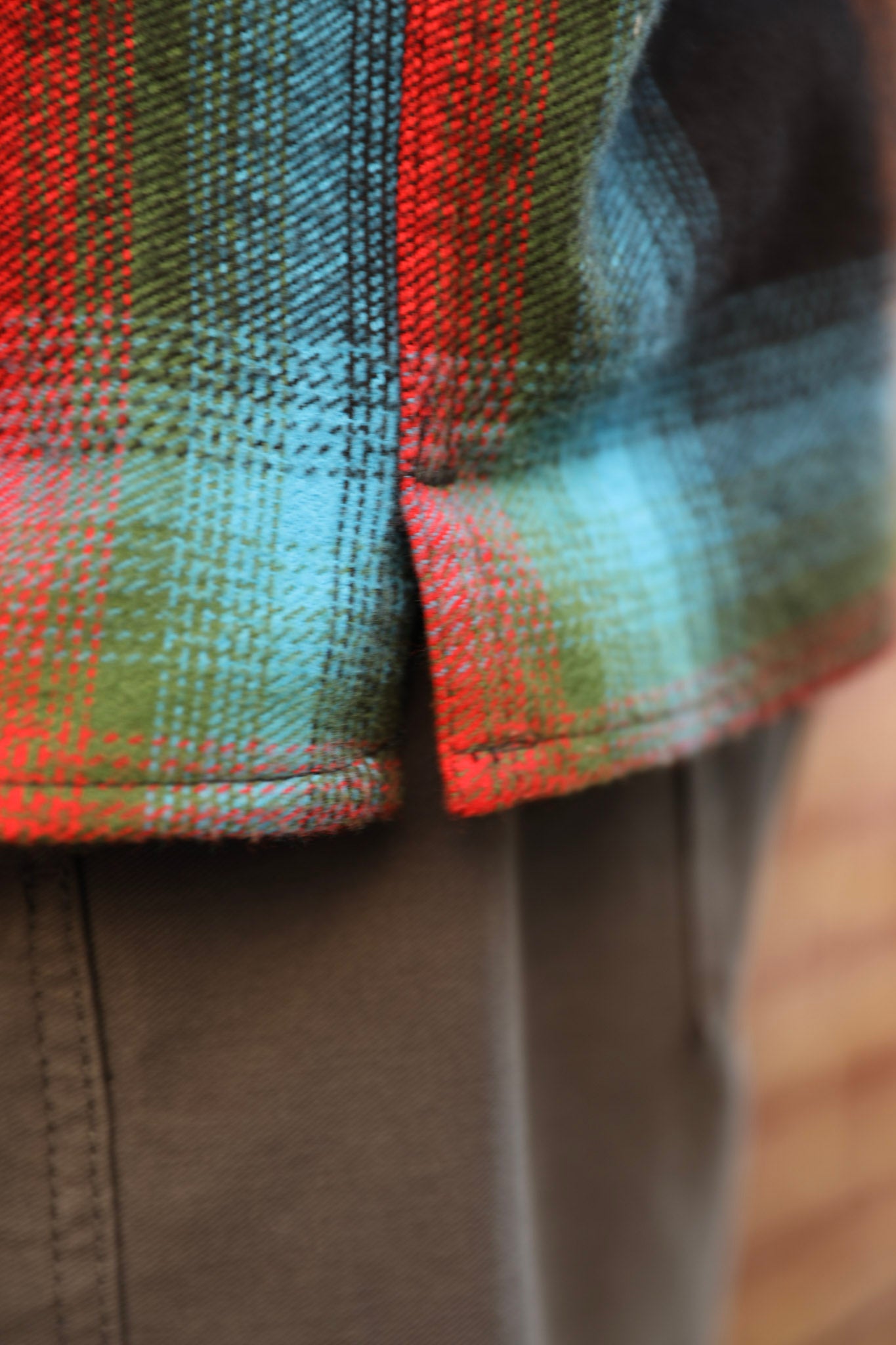 Close-up of a plaid flannel shirt with red, green, and blue tartan pattern, paired with brown pants.
