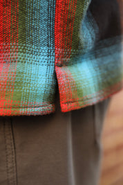Close-up of a plaid flannel shirt with red, green, and blue tartan pattern, paired with brown pants.