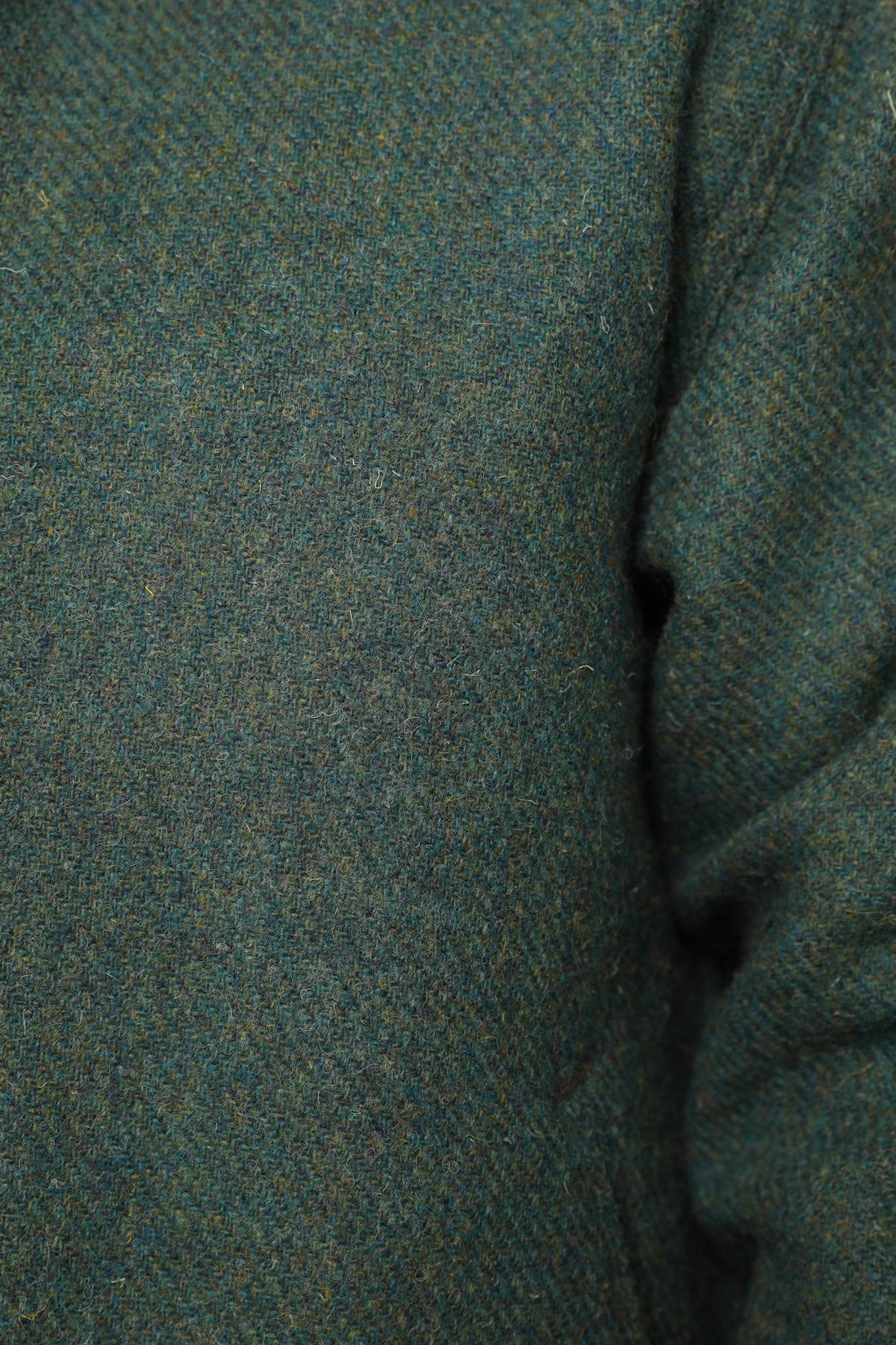 Close-up of a textured knit fabric in a heathered teal-green color, showing the weave and a folded seam on the right side.