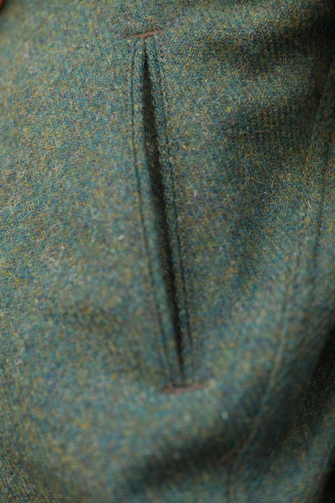 Close-up of a textured tweed fabric in a muted blue-gray color with a vertical welt pocket seam.